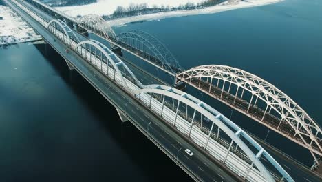 Auto-und-Zug-bewegt-sich-auf-einer-Brücke-über-einen-gefrorenen-Fluss-Luftbild-Drohne-Filmmaterial