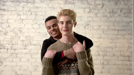 Happy-african-boy-hugging-his-beloved.-Happy-gay-couple,-lgbt-family,-white-brick-wall-on-background.-Close-up-60-fps