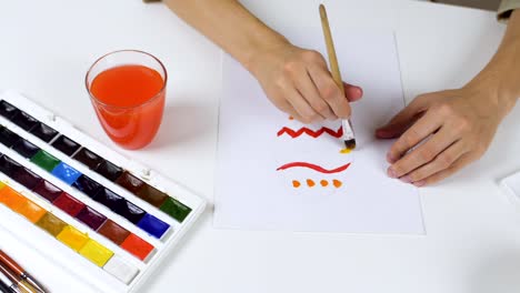 Unrecognizable-woman-paints-a-sketch-with-bright-colors-on-paper-for-an-Easter-card.-On-the-table-is-a-palette-with-paints-and-a-glass-of-water.