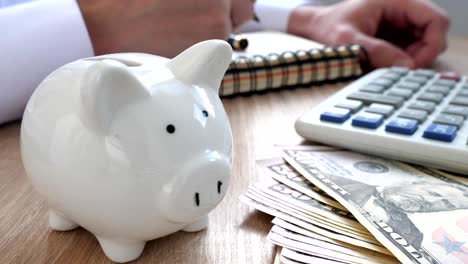 Savings-concept.-Piggy-bank,-calculator-and-man-writing-budget-in-a-note.