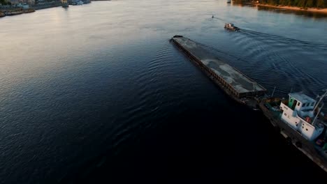 Barge-sails-along-the-river-near-the-city-port-on-sunset-aerial-footage