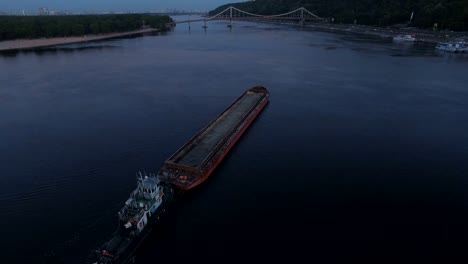 Barge-sails-along-the-river-near-the-city-port-on-sunset-aerial-footage