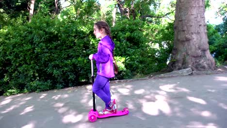 Little-child-learning-to-ride-a-scooter-in-a-city-park