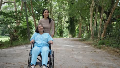 Mujer-mayor-con-su-hija-empujando-la-silla-de-ruedas-por-el-Parque