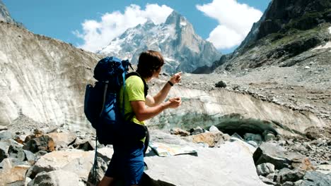 Tourist-man-with-a-backpack-exploring-the-route-on-the-map-and-phone-GPS,-adds-a-map-and-goes-on-a-route-in-the-mountain-hike