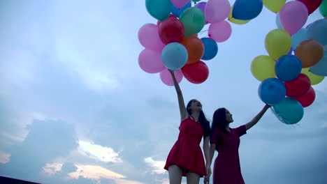 Two-girls-holding-balloon-with-sky-background-in-slow-motion.