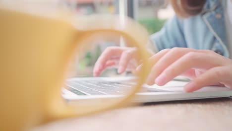 Business-freelance-Asian-woman-working,-doing-projects-on-laptop-and-drinking-warm-cup-of-coffee-while-sitting-on-table-in-cafe.-Lifestyle-smart-beautiful-women-working-concepts.