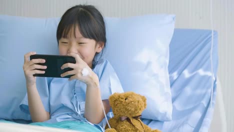 Niña-linda-acostado-en-cama-en-el-hospital,-viendo-dibujos-animados-divertidos,-películas-en-smartphone.-enfermedad-y-tratamiento.