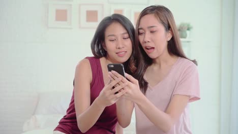 Young-Asian-women-lesbian-happy-couple-using-smartphone-checking-social-media-in-bedroom-at-home,-enjoy-love-moment-while-lying-on-bed-when-relaxed.-Lifestyle-LGBT-couple-together-indoors-concept.