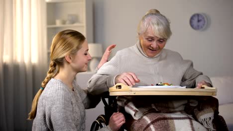 Female-volunteer-serving-dinner-to-handicapped-old-women,-elderly-sitter-service