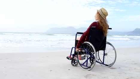 Rückansicht-des-junge-Behinderte-kaukasischen-Frau-mit-Hut-sitzt-im-Rollstuhl-am-Strand-4k