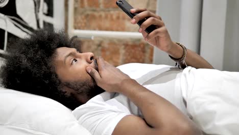 Hombre-africano-sorprendido-usando-smartphone-en-la-cama