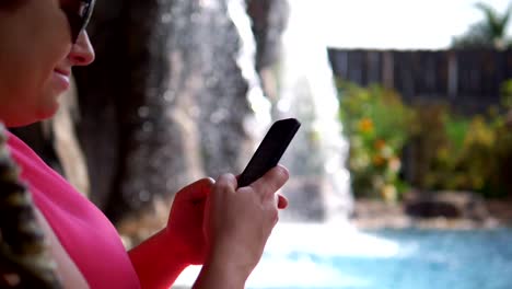 Woman-texting-on-smartphone-by-the-waterfall-in-a-park-in-slow-motion-180fps