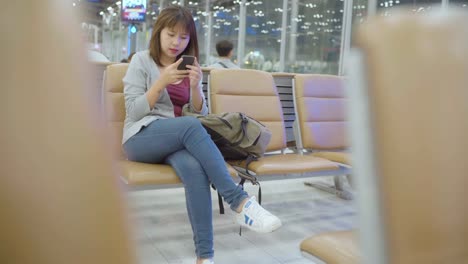 Asiatische-Frau-mit-Smartphone,-während-sie-auf-dem-internationalen-Flughafen-sitzt.