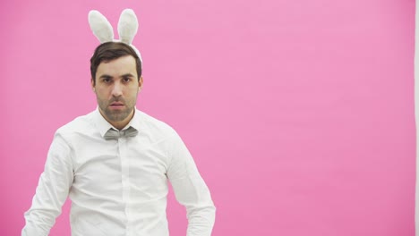 Young-man-standing-on-a-pink-background.-During-this-he-looks-at-the-camera-and-smokes-a-carrot.-After-putting-a-hand-on-the-arm.-The-guy-wears-a-bunny-ear.