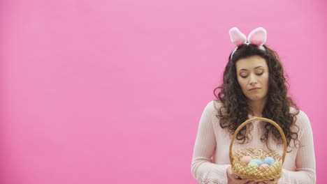 Ostern-Frau-Konzept.-Nettes-Mädchen-mit-Hasenohren-blickend-auf-ihren-Eierkarton-mit-bunten-Ostereier-isoliert-auf-rosa-Hintergrund.-Kopieren-Sie-den-Speicherplatz.