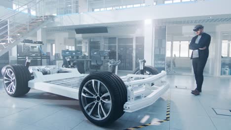 Automotive-Engineer-Working-on-Electric-Car-Chassis-Platform,-Using-Augmented-Reality-Headset.-In-Innovation-Laboratory-Facility-Concept-Vehicle-Frame-Includes-Wheels,-Suspension,-Engine-and-Battery.