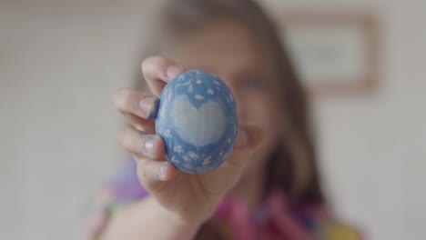 Cute-little-girl-holding-blue-easter-egg-with-painted-heart-in-hand