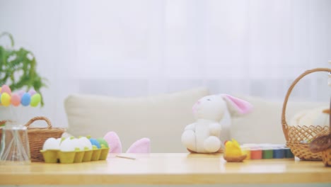 Young-adorable-girl-is-hiding-under-the-table-full-of-Easter-decorations-and-is-playing-with-Easter-bunny-in-his-hand.