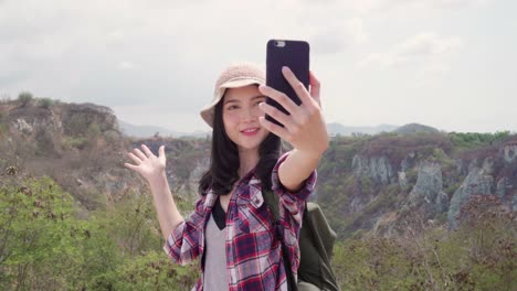 Blogger-Asian-backpacker-woman-record-vlog-video-on-top-of-mountain,-young-female-happy-using-mobile-phone-make-vlog-video-enjoy-holidays-on-hiking-adventure.-Lifestyle-women-travel-and-relax-concept.