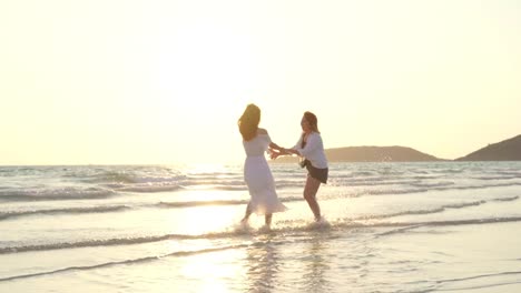 Junges-asiatisches-lesbisches-Paar-läuft-am-Strand.-Schöne-Freundinnen-freuen-sich,-sich-bei-Sonnenuntergang-am-Abend-am-Strand-am-Meer-zu-vergnügen.-Lifestyle-lesbisches-Ehepaar-reist-nach-Strandkonzept