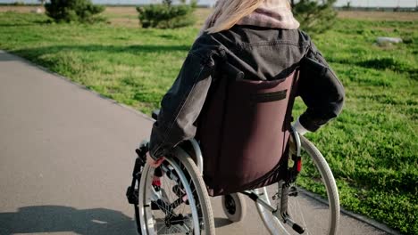 La-mujer-está-usando-silla-de-ruedas-para-moverse-al-aire-libre-en-un-día-soleado,-vista-trasera