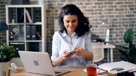 Excited-young-woman-playing-game-on-smartphone-touching-screen-at-work