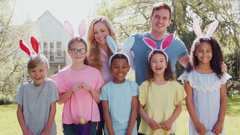 Portrait-of-group-of-parents-and-children-wearing-bunny-ears-on-Easter-egg-hunt-in-garden-smiling-at-camera---shot-in-slow-motion