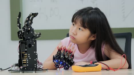 Little-Girl-is-playing-with-robotic-arm-in-a-school.-She-is-controlling-it-by-her-hand.