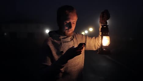 hombre-con-teléfono-y-linterna-de-queroseno-en-una-calle-de-niebla