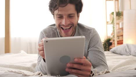 Joyful-man-using-digital-tablet-in-bed