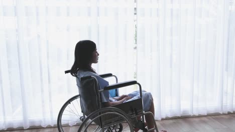 Mujeres-asiáticas-pacientes,-discapacitado-pierna-sentada-en-una-silla-de-ruedas-y-tiene-depresión-en-un-hogar-u-hospital-que-tiene-la-luz-del-sol-de-la-ventana.-Diapositiva-de-tiro-de-Dolly