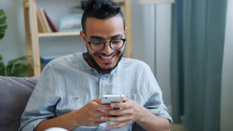 Glückliche-junge-Araber-mit-Smartphone-Blick-auf-Bildschirm-mit-glücklichen-Gesicht-zu-Hause