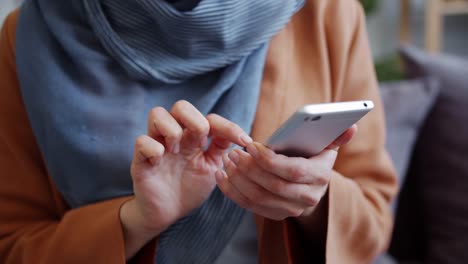 Toma-de-primer-plano-de-las-manos-femeninas-sosteniendo-el-teléfono-inteligente-tocando-la-pantalla-en-el-interior