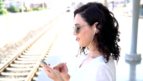 The-girl-is-waiting-for-the-train-at-the-subway-station-and-listening-to-music-on-headphones.-Use-smartphone-in-the-subway.-Underground.-Student-rides-the-subway.