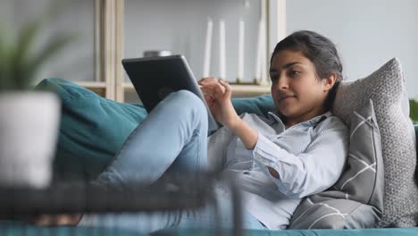 Glückliche-indische-Frau-entspannen-auf-Sofa-halten-mit-digitalen-Tablet