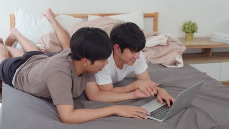 Asian-Gay-lgbtq-men-couple-using-computer-laptop-at-modern-home.-Young-Asia-lover-male-happy-relax-rest-together-after-wake-up,-watching-movie-lying-on-bed-in-bedroom-at-house-in-the-morning-concept.