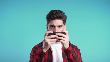 Handsome-man-playing-game-on-smartphone-on-blue-studio-wall.-Using-modern-technology---apps,-social-networks.-Slow-motion.