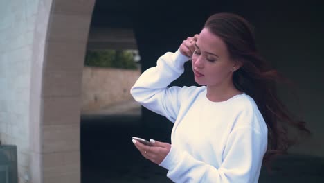 A-girl-stands-on-the-background-of-the-stone-arches-of-the-building,-holding-a-smartphone-in-her-hands.