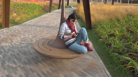 Caucasian-woman-sitting-on-a-round-park-bench-with-a-phone-in-her-hands