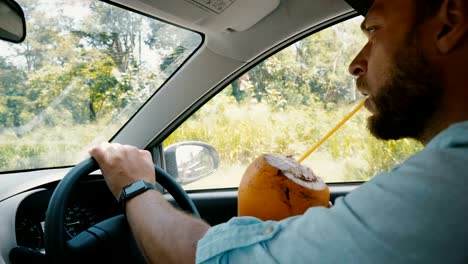 In-car-close-up-shot-of-relaxed-businessman-with-smart-watch-driving-car,-enjoying-exotic-fruit-drink-on-summer-vacation