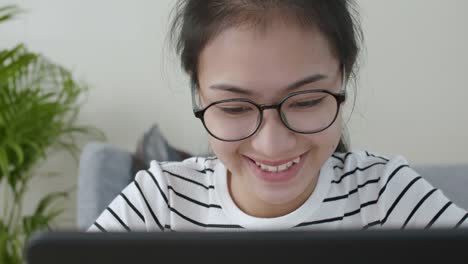 Primer-plano-de-la-mujer-asiática-cara-Gafas-de-desgaste-usando-un-ordenador-portátil-y-sonrisa-feliz,-aprendizaje-en-línea-en-el-concepto-de-casa