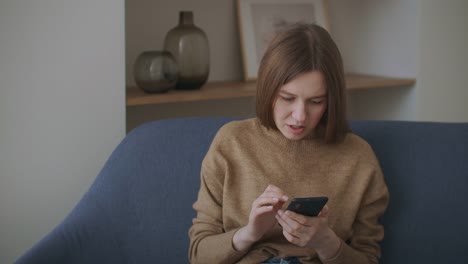 business-woman-typing-message-on-mobile-phone-at-home-office.-Young-girl-chatting-on-phone-in-slow-motion.-Close-up-young-woman-hands-using-smartphone-on-couch.