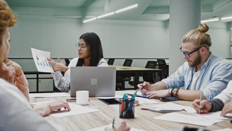 Businesswoman-Chefin-vermittelt-ideenfördernde-Ideen-für-Startup-Projekt-an-verschiedene-Kollegen-beim-Brainstorming,-sitzt-am-Tisch-im-Büro