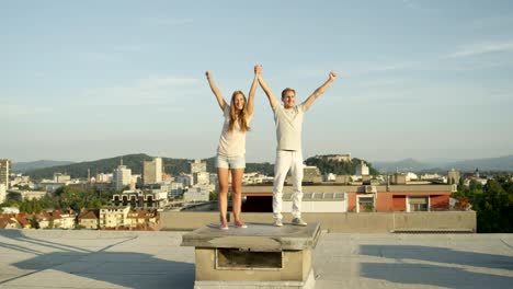 CLOSE-UP:-Happy-young-couple-standing-on-rooftop-and-raising-hands-in-the-sky