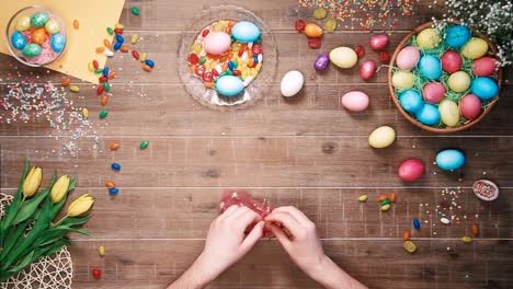 Man-putting-candys-in-the-bag-on-table-decorated-with-easter-eggs.-Top-view