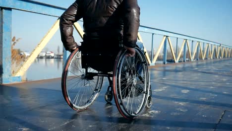 Disabled-man-in-wheelchair-pushing-himself-outdoors-on-bridge