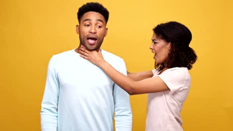 Angry-young-african-woman-strangling-her-boyfriend-isolated-over-yellow-background