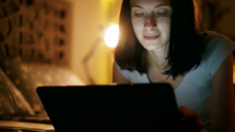 Close-up-of-young-attractive-woman-using-tablet-computer-at-night-time-lying-in-bed-at-home