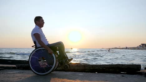 lisiado-hombre-empuja-a-sí-mismo-en-el-mar-de-fondo-puesta-de-sol-y-disfrutar-de-la-naturaleza,-persona-discapacitada-en-silla-de-ruedas